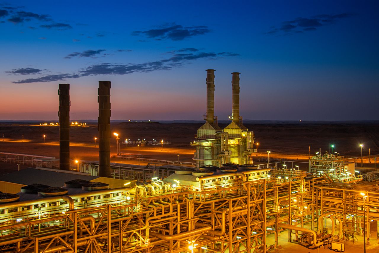Services Aerial view of an illuminated factory with chimneys at sunset, showcasing industrial architecture.