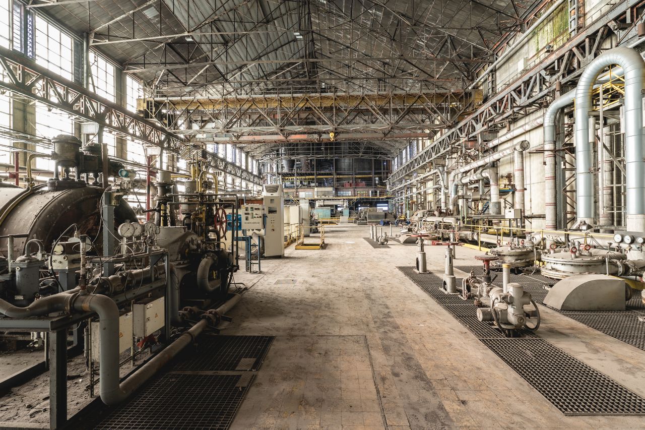 Home Spacious industrial warehouse interior featuring machinery and network of pipes.