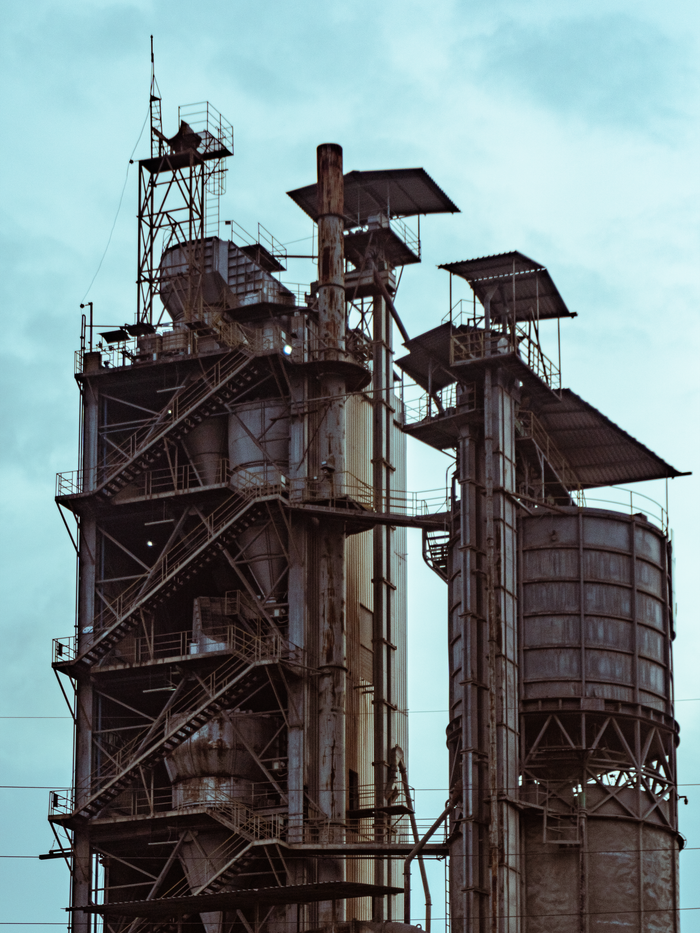 Services A close-up view of industrial factory towers with a clear blue sky background.